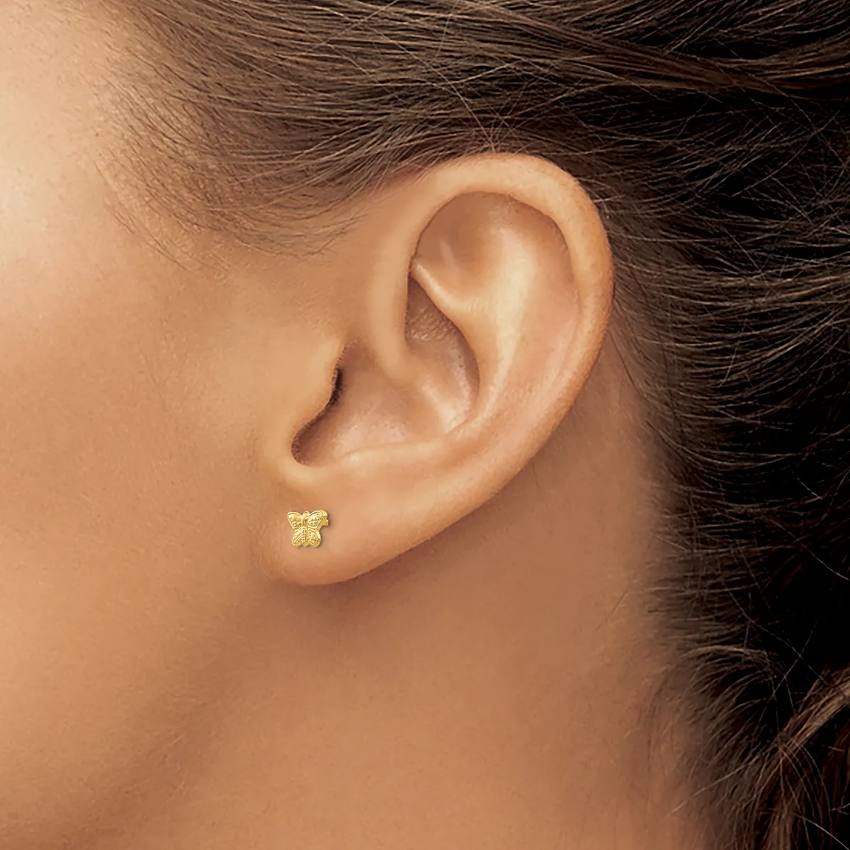 A small gold stud earring with a textured square design worn in a pierced earlobe.