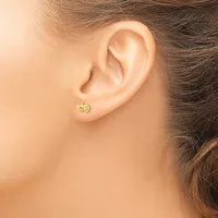 A person wearing a small gold stud earring with a textured circular face in their earlobe.