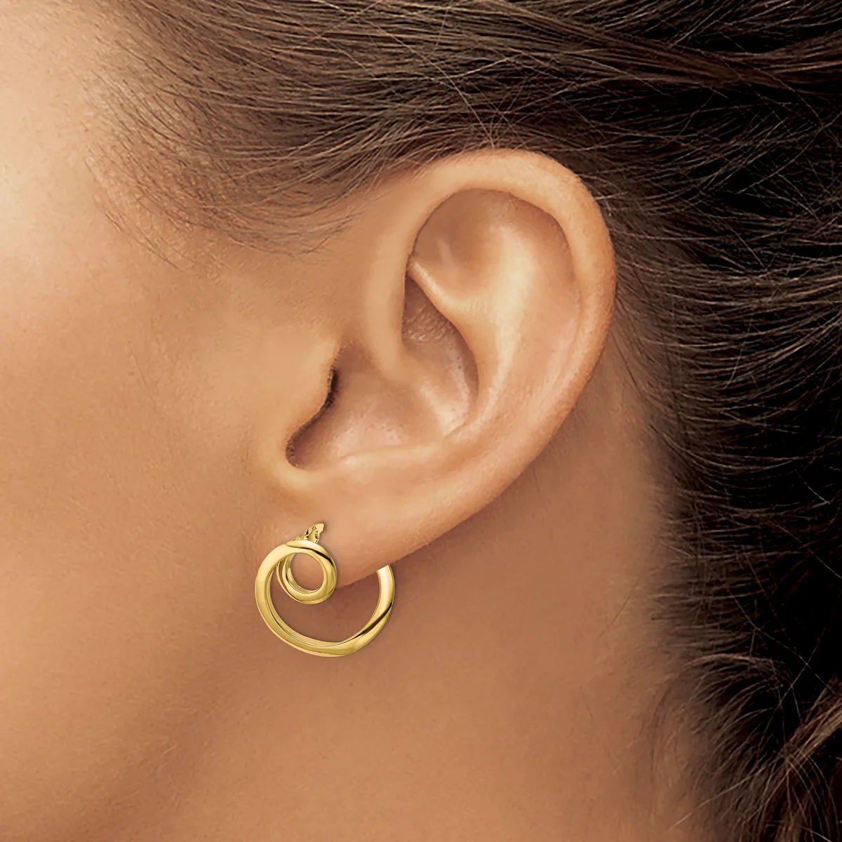 A gold spiral hoop earring worn on a person's earlobe, shown from the side against their neck and shoulder.
