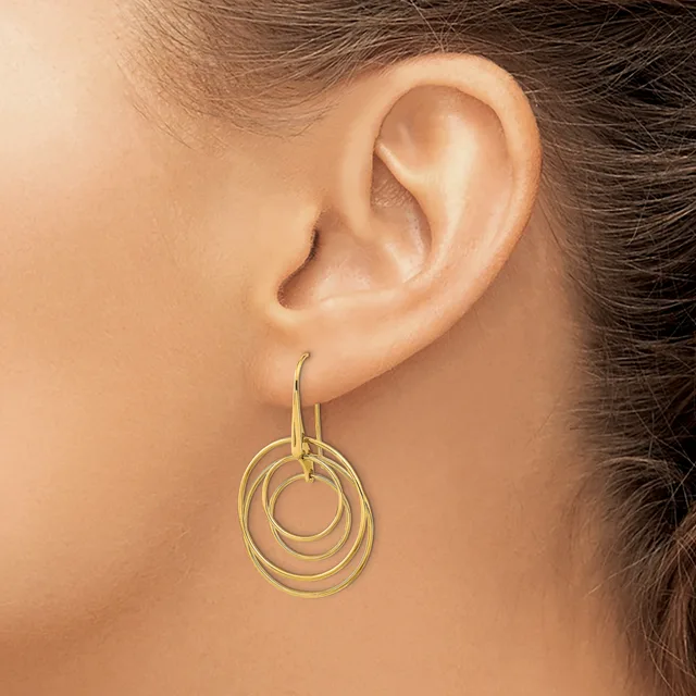 A woman wearing a gold-toned concentric circular dangle earring on a hook, shown from the side view of her ear and neck.