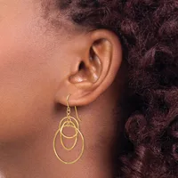 A person wearing gold-toned nested oval hoop earrings on fish hook wires, shown in profile against their ear and shoulder.