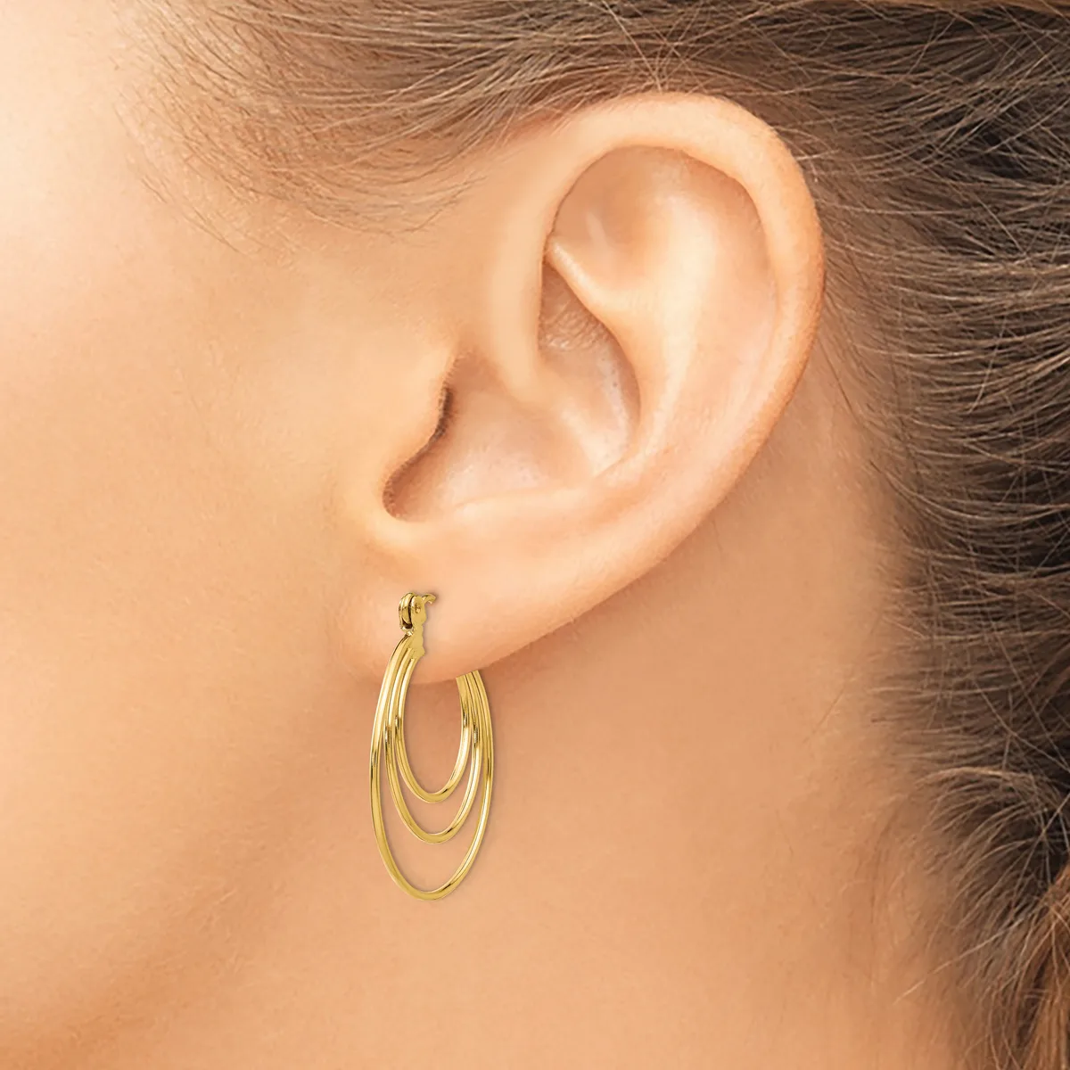 A woman wearing triple-loop gold hoop earrings with a brushed finish, shown from the side profile of her ear.