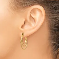 A woman wearing triple-loop gold hoop earrings with a brushed finish, shown from the side profile of her ear.