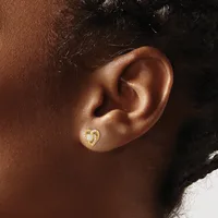 A close-up of a person's ear wearing a small gold heart-shaped stud earring with a white pearl or opal center.