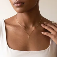 A woman wearing a white sleeveless top displays a gold chain necklace with a small cross pendant resting at her collarbone.