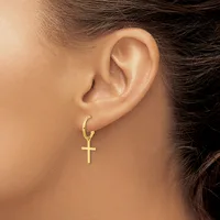 A gold hoop earring with a dangling cross pendant worn on a person's earlobe, shown from the side profile.
