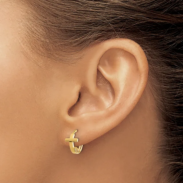 A person wearing a small gold cross hoop earring in their earlobe, shown from the side profile.