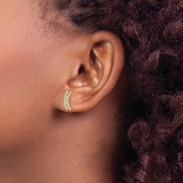 A person wearing a gold curved hoop earring with small gemstone settings on the lower lobe of their ear.