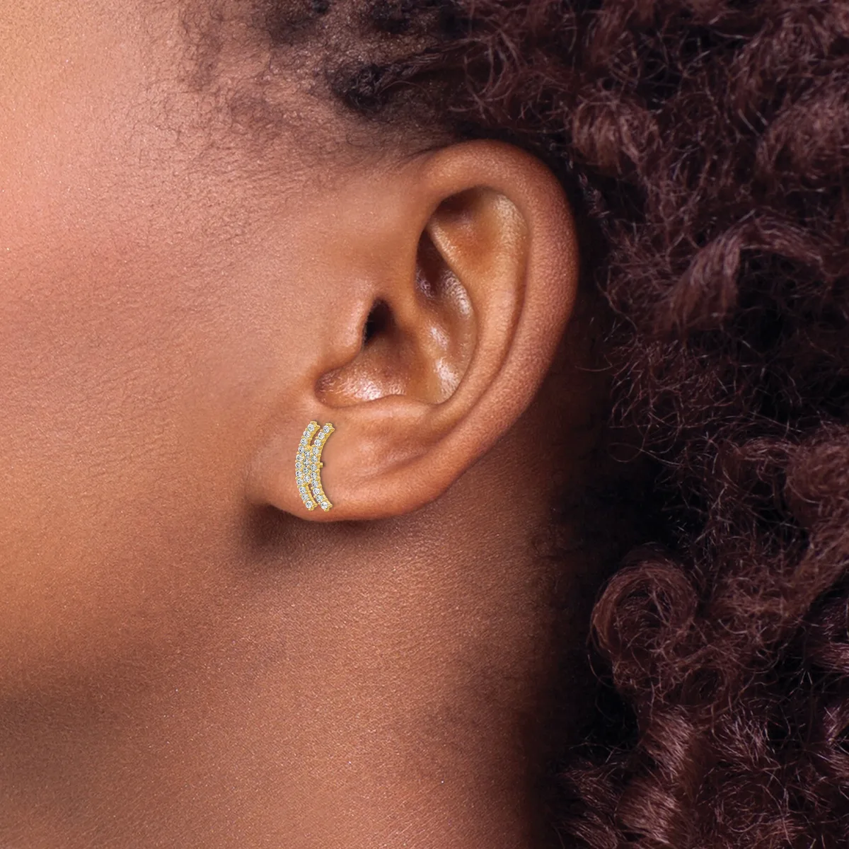 A person wearing a gold curved hoop earring with small gemstone settings on the lower lobe of their ear.