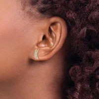 A person wearing a gold curved hoop earring with small gemstone settings on the lower lobe of their ear.
