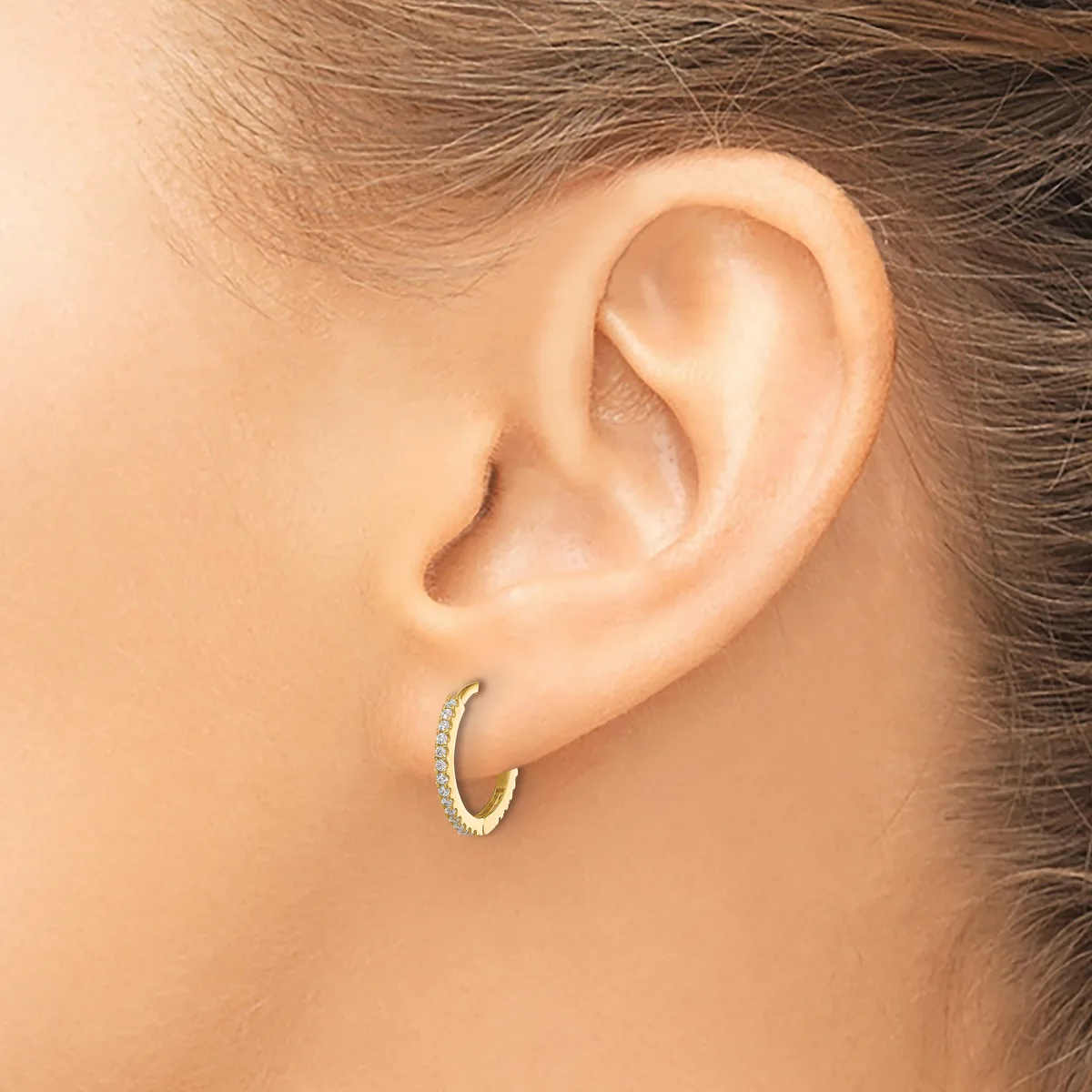 A gold hoop earring with diamond accents worn in a woman's earlobe, shown from a side view.