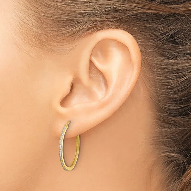 A person wearing two-tone hoop earrings with a textured outer surface and smooth inner band, shown from the side profile of their ear.