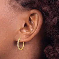 A person wearing a gold hoop earring in their earlobe, shown in profile against their shoulder and dark curled hair.