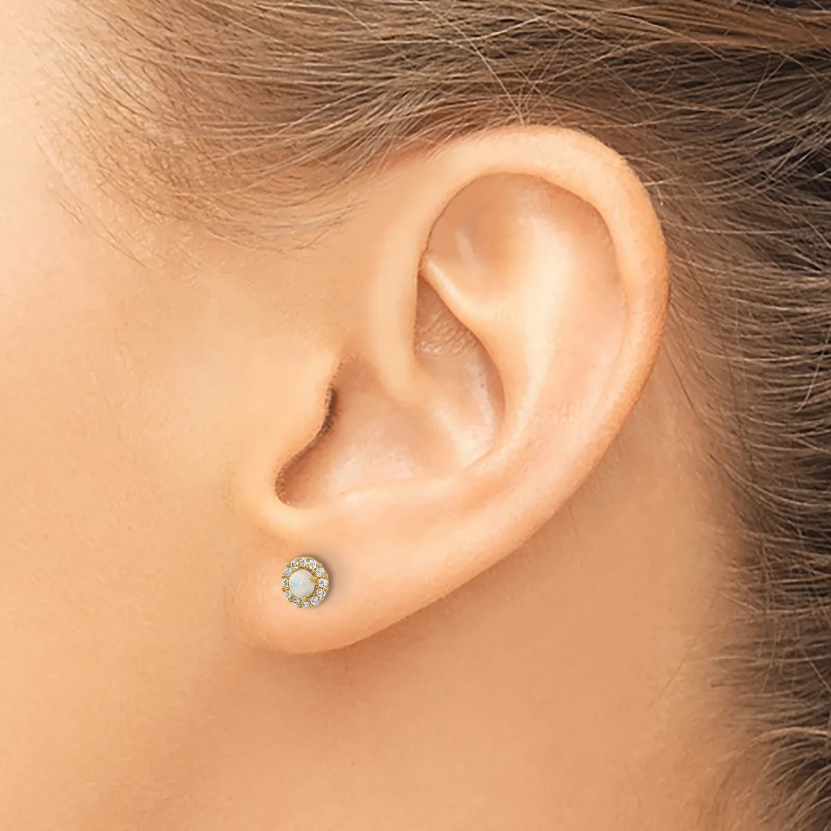 A person wearing a small round stud earring with a pale stone center surrounded by small diamonds in a white metal setting.