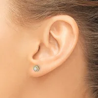 A person wearing a small round stud earring with a pale stone center surrounded by small diamonds in a white metal setting.