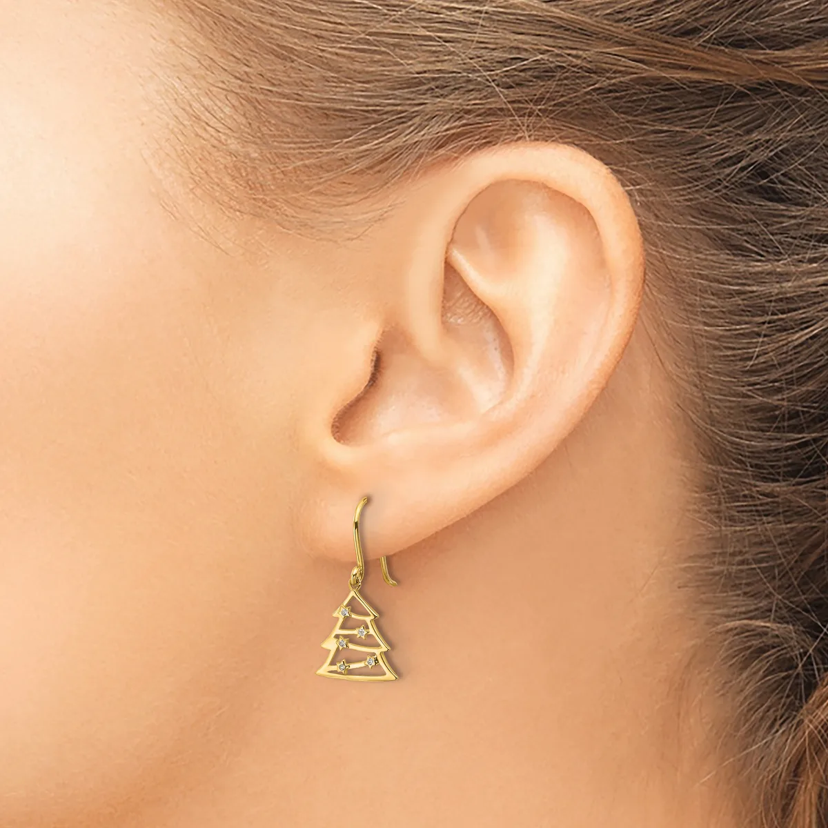 A person wearing a gold-toned triangular tree-shaped dangle earring on a fish hook wire, shown from the side view of their ear.