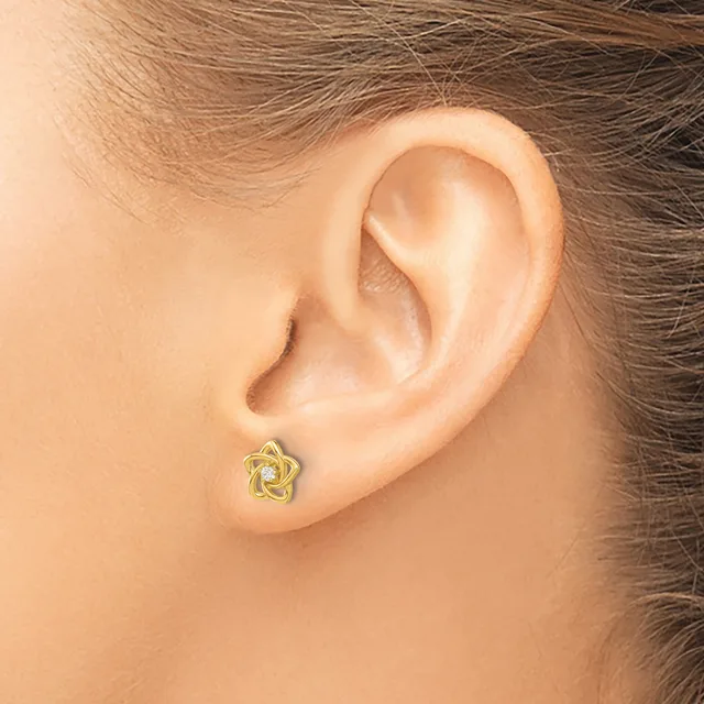 A small gold star-shaped stud earring with an open twisted design worn on a person's earlobe.