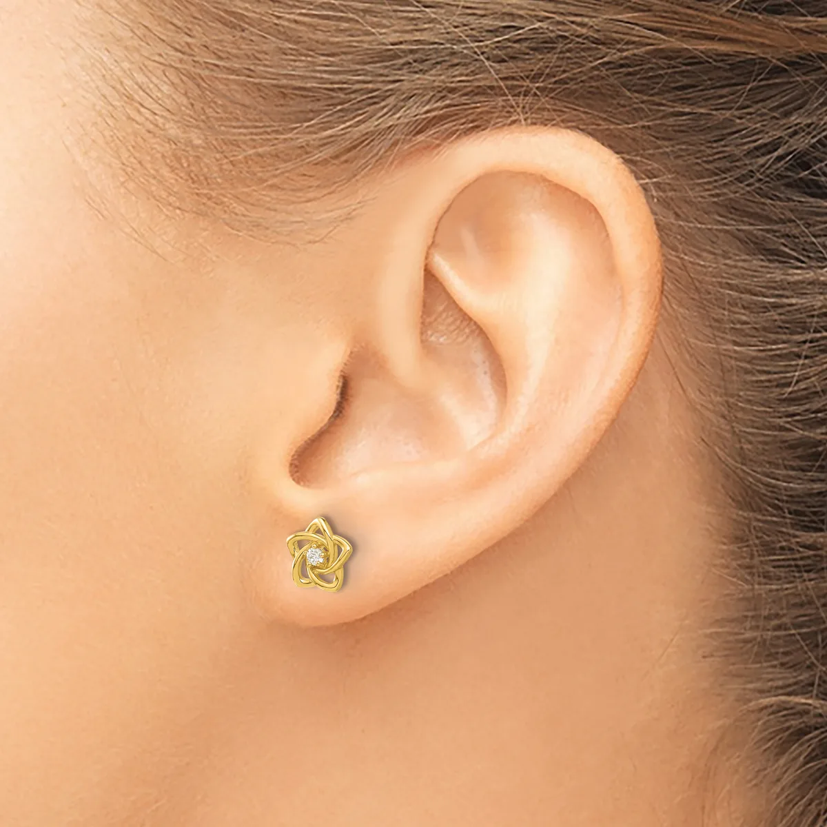 A small gold star-shaped stud earring with an open twisted design worn on a person's earlobe.