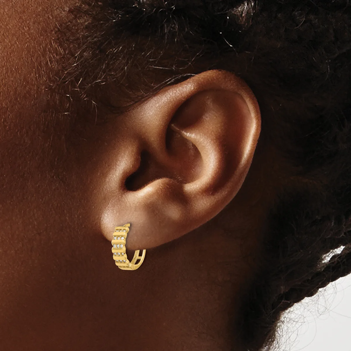 A small gold hoop earring with a textured surface worn on the earlobe of a person with brown skin and dark hair.