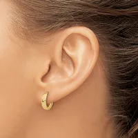 A small gold hoop earring with a textured surface worn on the earlobe of a person with brown hair.