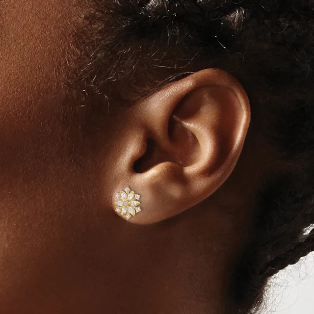 A gold flower-shaped stud earring with white gemstones worn on a person's earlobe.
