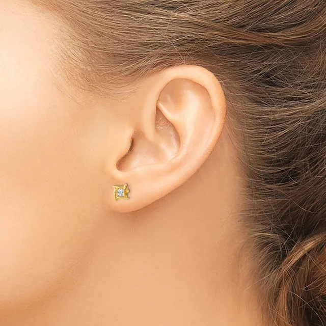 Close-up of a person's ear wearing a small square stud earring with a clear stone set in a pale metal, shown from the side profile.