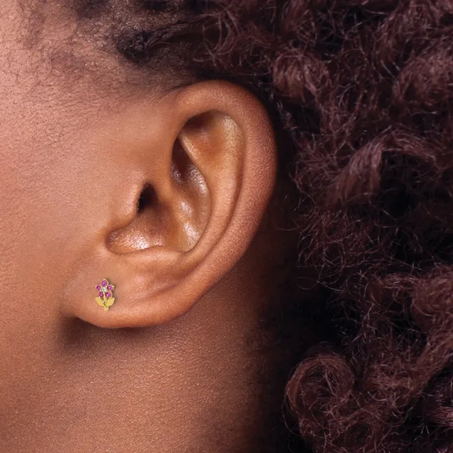 A person wearing a small stud earring with a pink stone and yellow metal detail in their earlobe.