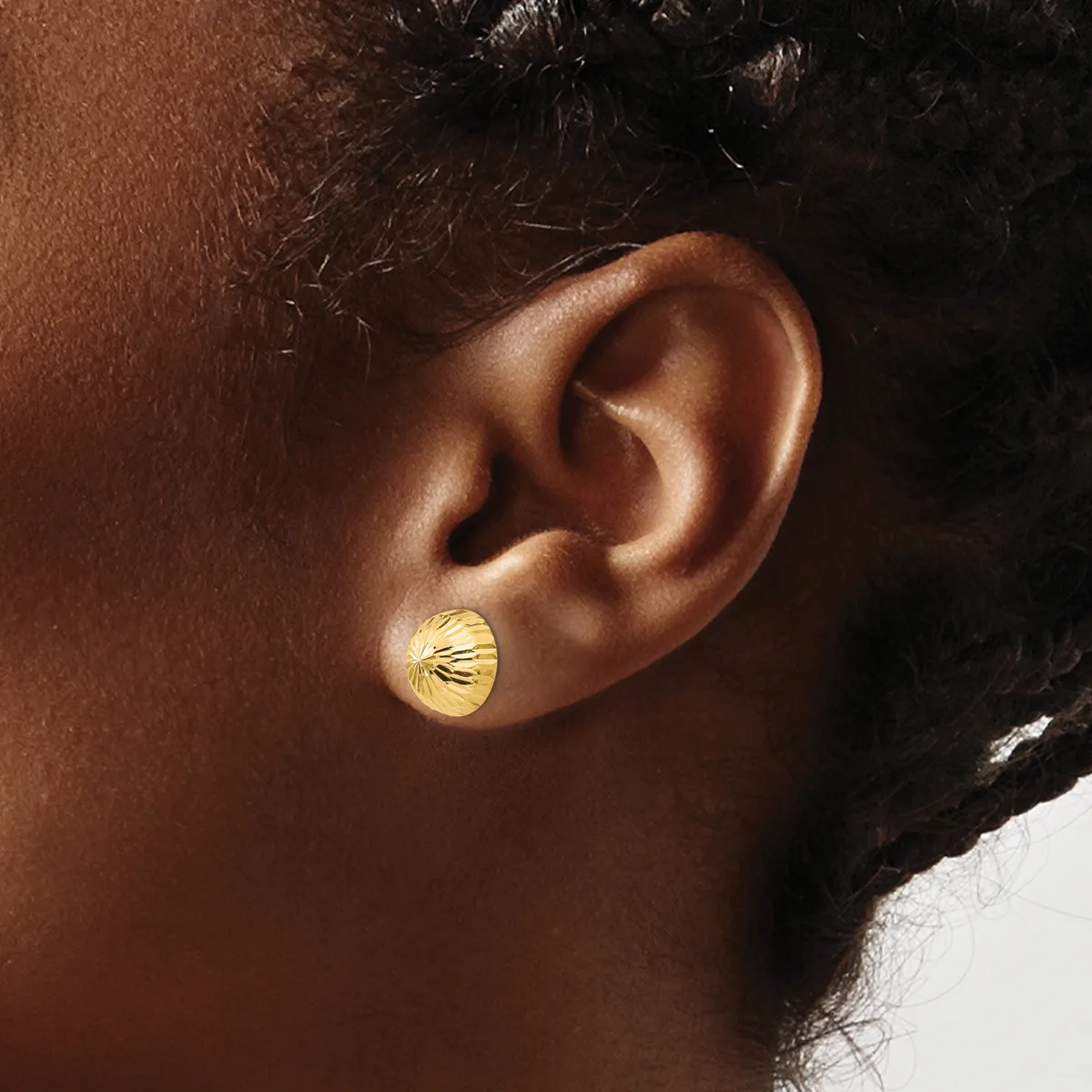 A person wearing a small gold stud earring with a ridged shell or fan design in their earlobe.