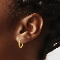 A close-up side view of a person's ear wearing a small gold hoop earring with a textured finish.