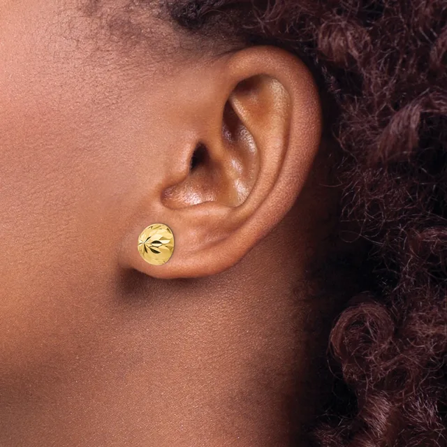 A person wearing a small round gold stud earring with a textured surface in their earlobe, shown in profile view.