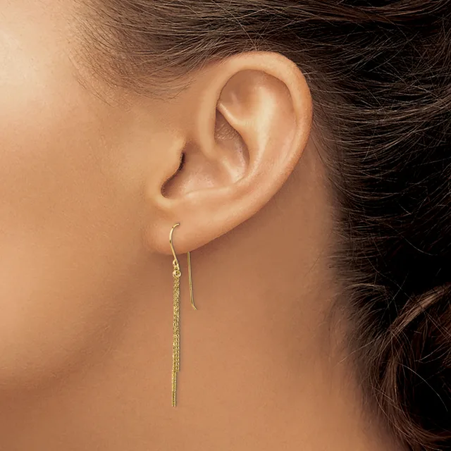A person wearing a long, delicate chain threaded earring in gold-toned metal that hangs straight down from the earlobe.