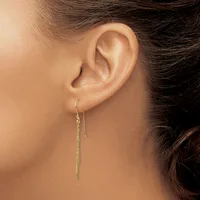 A person wearing a long, delicate chain threaded earring in gold-toned metal that hangs straight down from the earlobe.