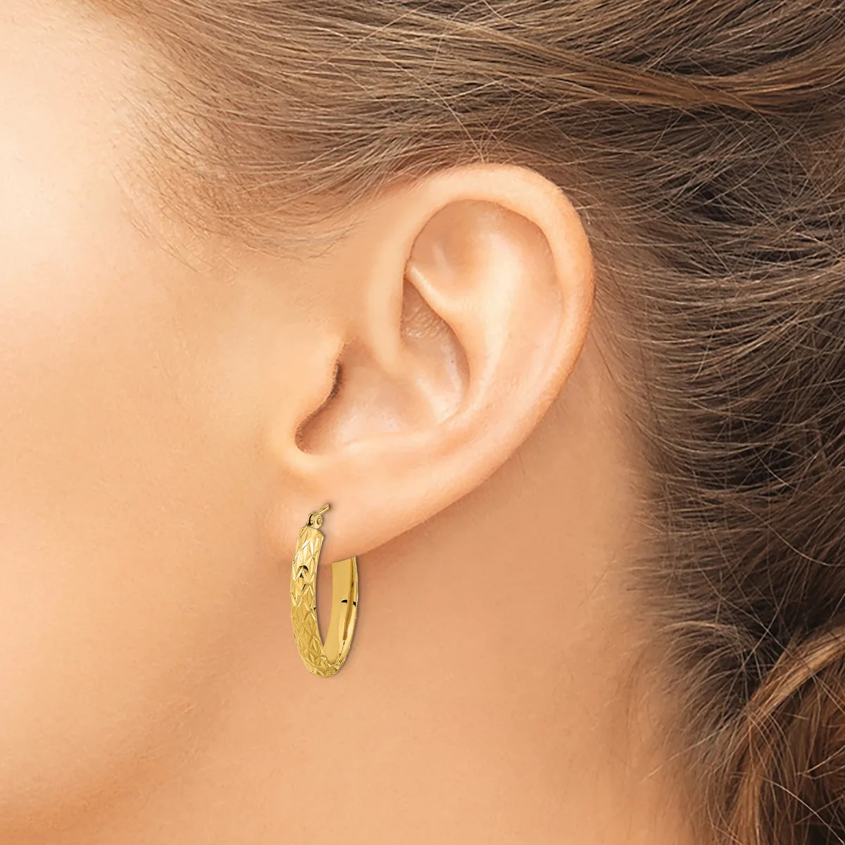 A person wearing small gold hoop earrings with a textured surface, shown from the side view of their ear.