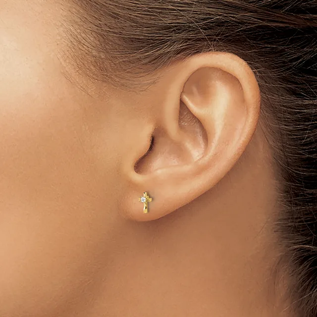 A person wearing a small gold cross earring with gemstones in their earlobe, shown from the side profile of their head and ear.