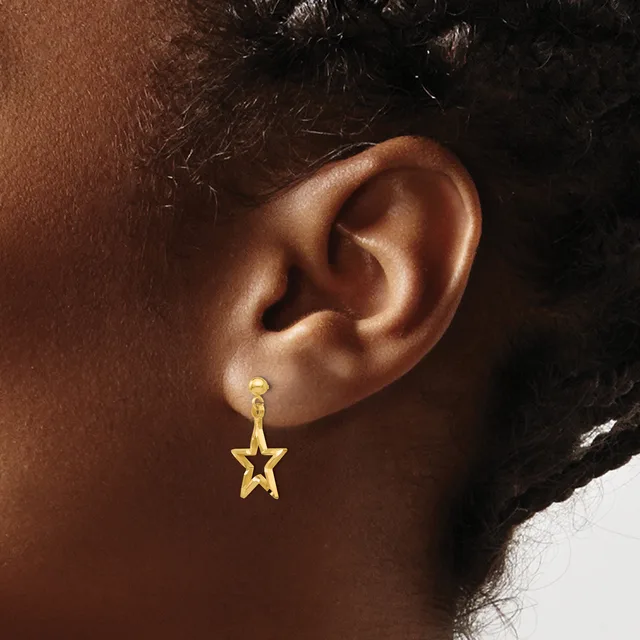 A gold star-shaped dangle earring hangs from a post on the earlobe of a person with brown skin and dark hair.