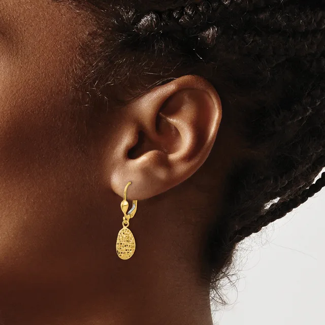 A person wearing a gold hoop earring with a textured oval pendant hanging from it.