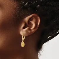 A person wearing a gold hoop earring with a textured oval pendant hanging from it.