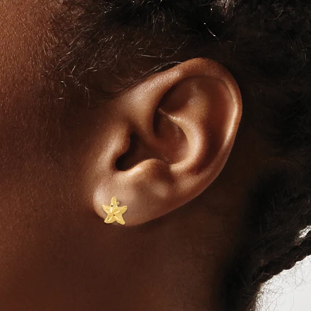 A small gold star-shaped stud earring worn in the earlobe of a person with medium brown skin tone.