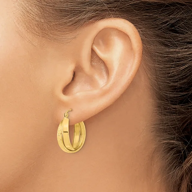 A woman wearing gold hoop earrings with a textured finish, shown from the side profile of her face and ear.