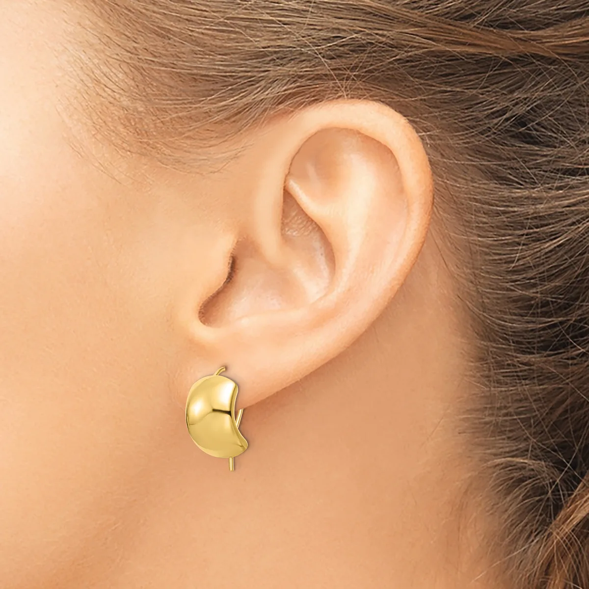 A polished gold curved earring with a post back worn on a person's earlobe, shown from the side view.