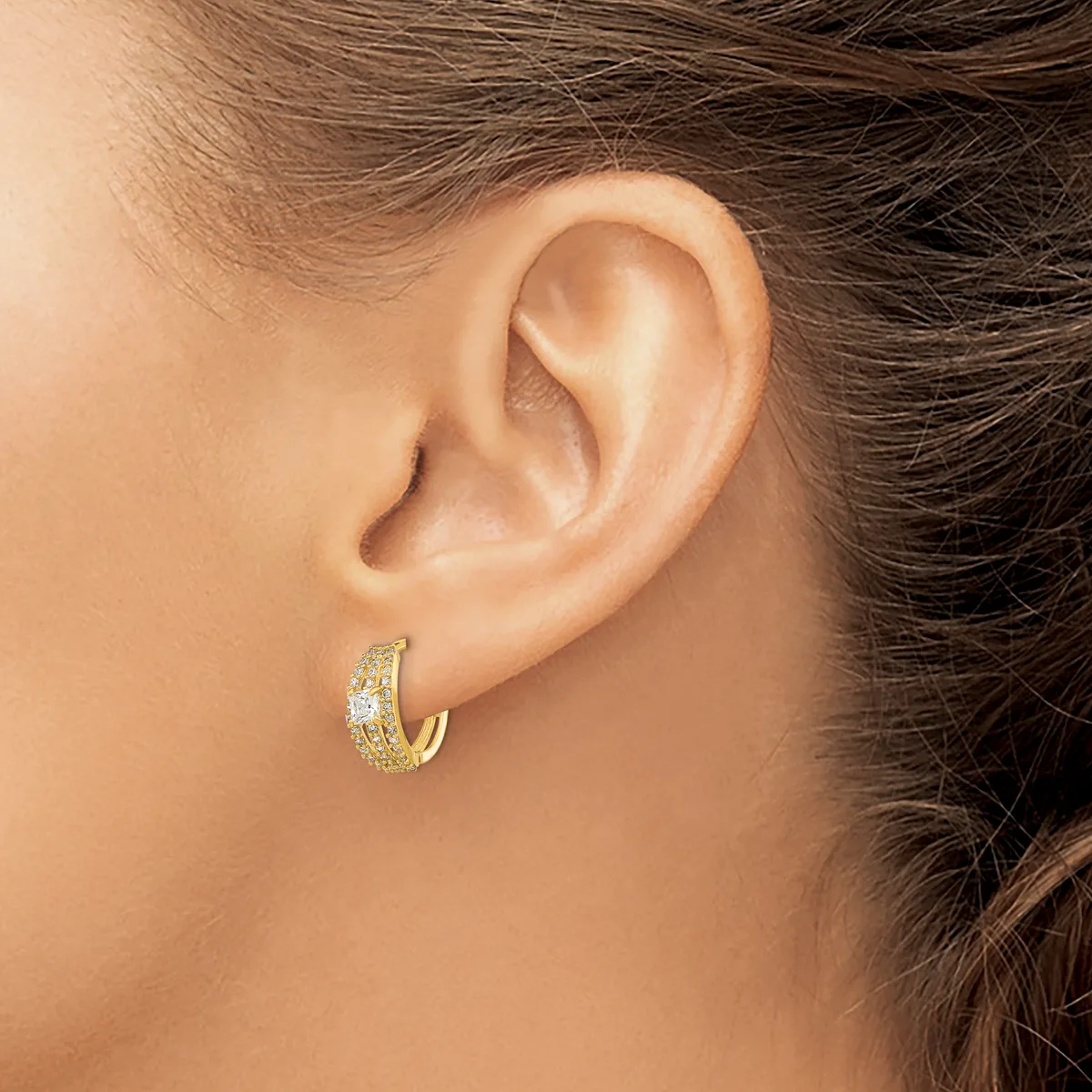 A person wearing a gold hoop earring with a textured or hammered finish on their earlobe.