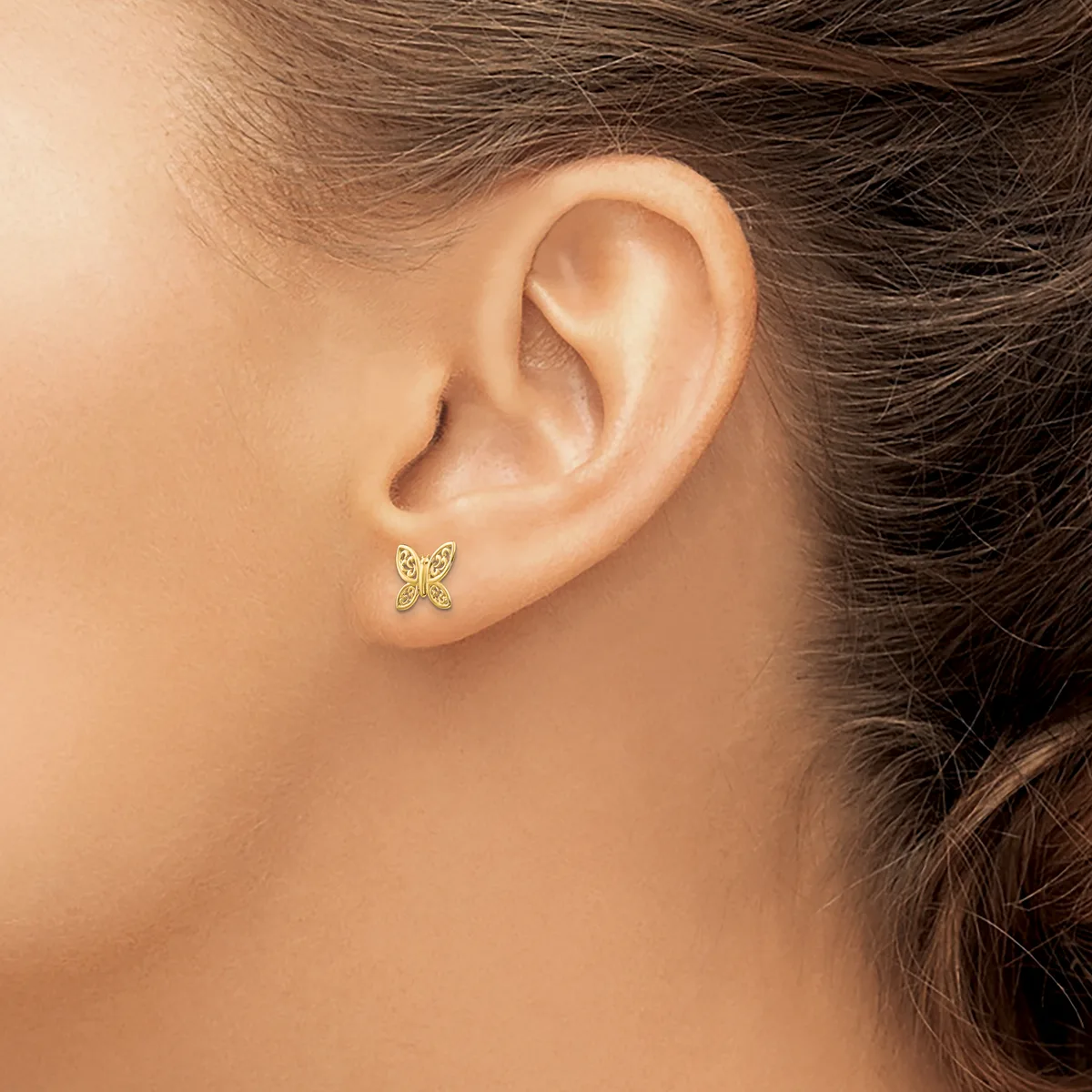 A small gold butterfly stud earring with textured wings shown worn on a woman's earlobe.