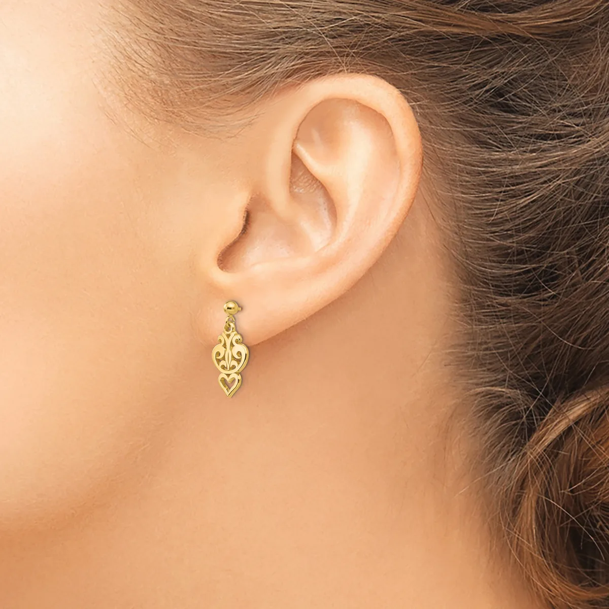 A woman wearing a gold filigree drop earring with an ornamental leaf-shaped design hanging from her earlobe.