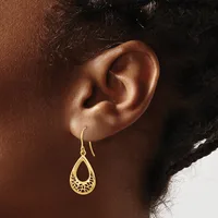 A person wearing a gold teardrop-shaped filigree earring with a fish hook closure on their earlobe.