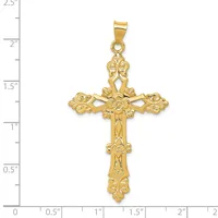 A gold ornate cross pendant with decorative filigree details and a small stamped hallmark, shown next to a ruler measuring approximately 2.25 inches in length.