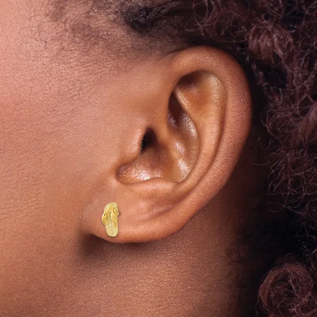 A close-up view of a person's ear wearing a small gold-colored stud earring with a textured, leaf-like shape.