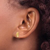 A close-up view of a person's ear wearing a small gold-colored stud earring with a textured, leaf-like shape.
