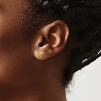A person wearing a small gold smiley face stud earring in their earlobe, shown in profile against a neutral background.