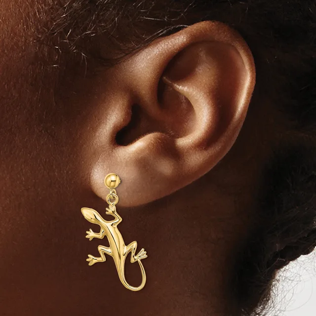 A gold lizard-shaped dangle earring worn on a person's earlobe, shown from the side.