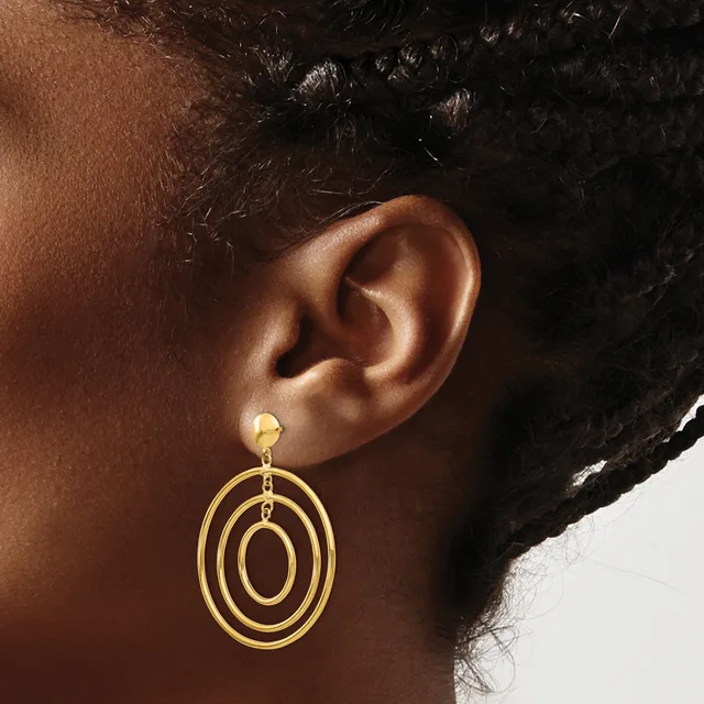 A person wearing a gold-toned dangle earring with concentric oval rings, shown from the side view of their ear and neck.
